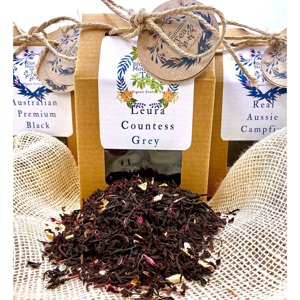 Tea Packaging for B;ue Mountains TEa Co, shows three boxes of tea with Leura Countess Grey in the middle and a sprinkling of Leura Countess Grey Tea in front of the boxes. All boxes are recycled Kraft Boxes and decorated to make lovely gifts.  